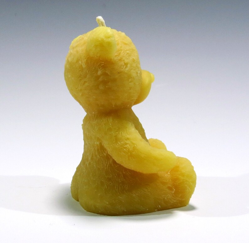May include: A yellow, bear-shaped candle with a white wick. The candle is sculpted in a sitting position, with its arms gently curved. The bear has a textured surface, giving it a soft appearance. This decorative candle is suitable for home decor.