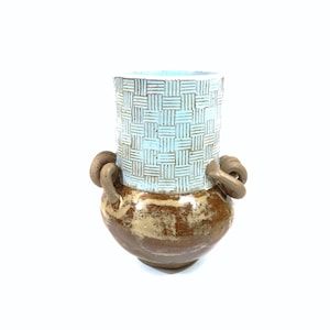May include: A ceramic vase with two handles, a light blue top with a woven pattern, and a brown bottom with a speckled glaze.