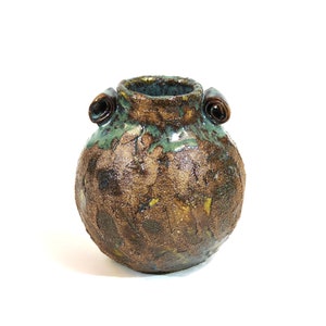 May include: A small, round, brown ceramic vase with a green glaze and two rolled handles. The vase has a rustic, textured surface.