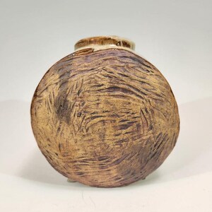 May include: A small, round, brown ceramic vase with a textured surface. The vase has a white rim and a slightly flared opening.