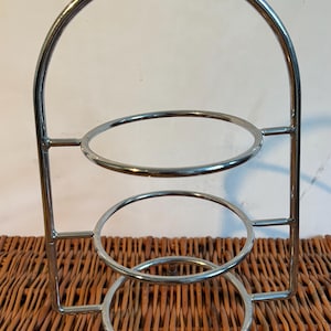 Könnte beinhalten: Ein dreistöckiger Servierständer aus Chrom mit einem Griff. Der Ständer ist aus Metall und hat einen runden Sockel.