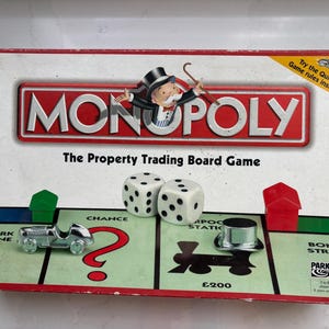 May include: A Monopoly board game box featuring the classic logo, Rich Uncle Pennybags, and the text The Property Trading Board Game. The box displays two white dice, a silver race car token, a silver top hat token, a green house, and a red house.