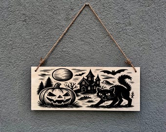 May include: Wooden Halloween sign with a carved design of a jack-o'-lantern, haunted house, full moon, bats, and a black cat. The rectangular sign hangs from a jute rope. The design is in black and white.