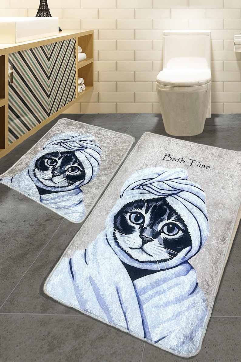 K&ouml;nnte beinhalten: Zwei Badematten mit einem Katzendesign. Die gr&ouml;&szlig;ere Matte hat den Text "Bath Time" darauf. Die Katze tr&auml;gt ein Handtuch und hat einen s&uuml;&szlig;en Gesichtsausdruck.