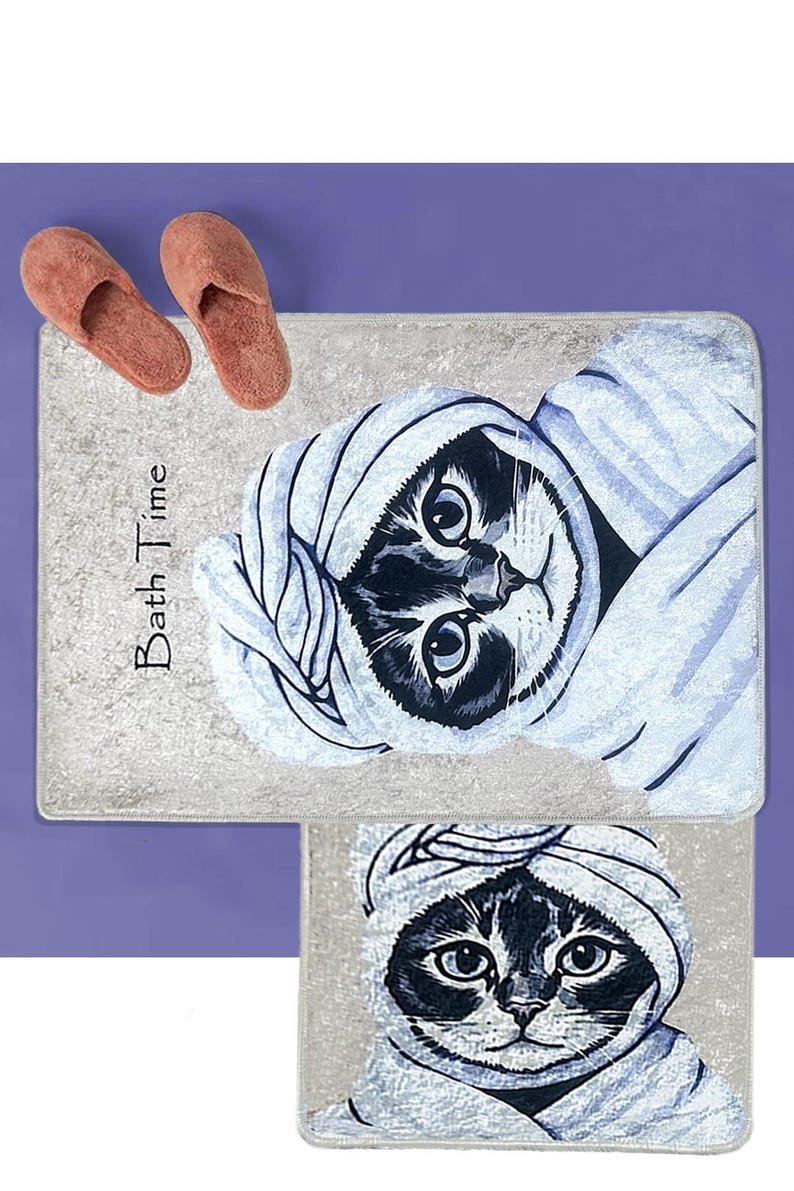 K&ouml;nnte beinhalten: Zwei Badematten mit grauem Hintergrund und einer Schwarzwei&szlig;illustration einer Katze, die ein Handtuch tr&auml;gt. Die obere Matte hat den Text "Bath Time" aufgedruckt.
