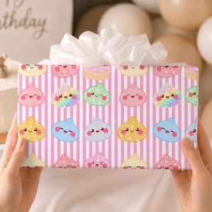 May include: A rectangular gift box wrapped in pink and white vertical striped paper featuring a repeating pattern of smiling, colorful dumpling characters with glittery textures, topped with a large, white, multi-looped decorative ribbon bow.