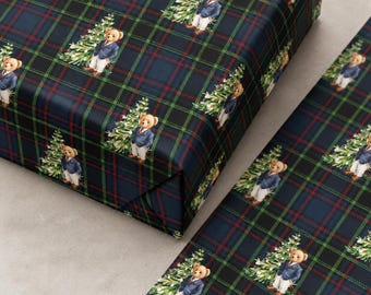 May include: Wrapping paper featuring a repeating pattern of teddy bears wearing navy blue blazers and white trousers, each standing next to a green pine tree. The background consists of a dark blue, green, and red plaid tartan grid design.
