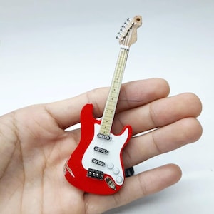 Puede incluir: Una guitarra eléctrica roja y blanca con un acabado desgastado. La guitarra tiene una golpeador blanco y seis cuerdas.