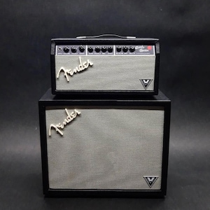 Könnte beinhalten: Ein schwarzes und graues Fender Gitarrenverstärker- und Lautsprecherbox-Set. Der Verstärker hat mehrere Knöpfe und das Fender-Logo in weißer Schrift. Die Lautsprecherbox hat eine graue Gitterfront und ein passendes Fender-Logo. Ein V-förmiges Logo ist auf beiden vorhanden.