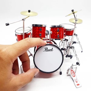 May include: A miniature red drum kit with a bass drum that says "Pearl" on the front. The kit includes a bass drum, two toms, a snare drum, and two cymbals.