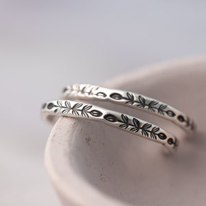 Pode incluir: Duas pulseiras de prata com um delicado design de folhas. As pulseiras est&atilde;o empilhadas uma em cima da outra e est&atilde;o em uma tigela branca.