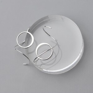 Funky silver earrings shown on a gray surface, the earrings are both shown one is facing front and the other is upside down to show off the sculpted wire design.