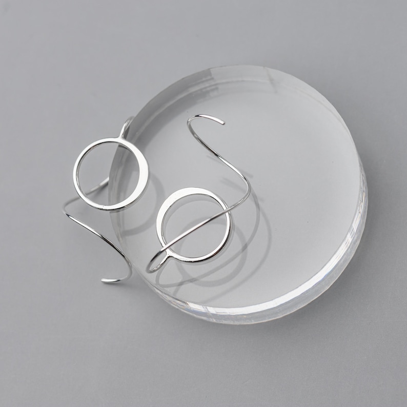 Funky silver earrings shown on a gray surface, the earrings are both shown one is facing front and the other is upside down to show off the sculpted wire design.