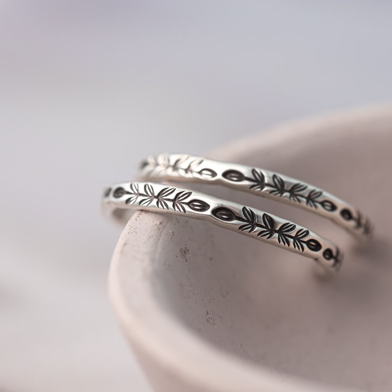 Pode incluir: Duas pulseiras de prata com um delicado design de folhas. As pulseiras est&atilde;o empilhadas uma em cima da outra e est&atilde;o em uma tigela branca.