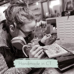 Handmade sterling silver jewelry handcrafted in Connecticut by a small business.  This image shows a woman using a torch to solder silver jewelry in a home studio.