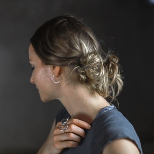 Side profile of a model wearing one inch sterling silver hoops.  This shows how they appear to go all of the way through and around the ear as the ear nut and gap are hidden behind the ear.  The earrings reflect the light and are highly polished.