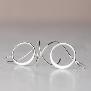 A pair of sterling silver earrings is shown laying on a surface to show off their dimensional design.  These earrings feature a hammered silver circle and a spiral ear wire