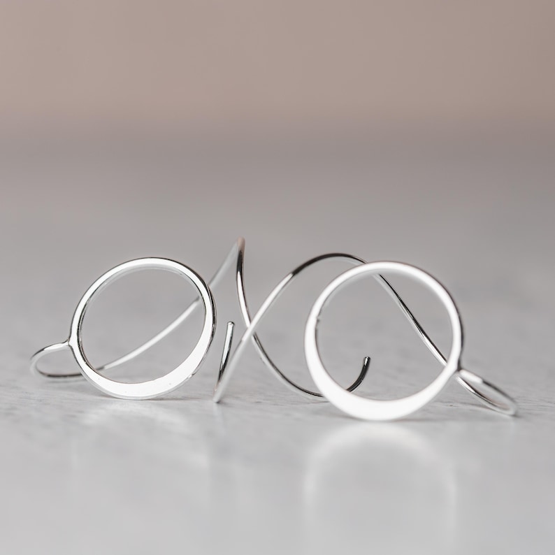 A pair of sterling silver earrings is shown laying on a surface to show off their dimensional design.  These earrings feature a hammered silver circle and a spiral ear wire