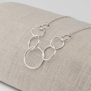 May include: A silver necklace with a chain and multiple interconnected circles of varying sizes.