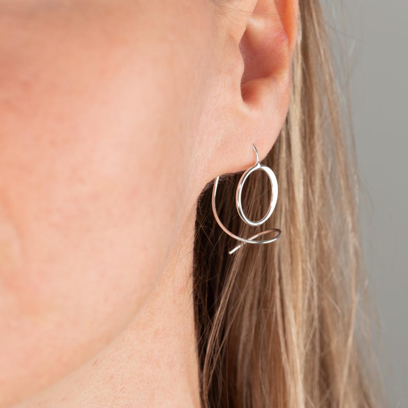 sterling silver earrings being worn on a model.  This is a close up of the earring which features a hand hammered small circle that connects to a spiral ear wire that threads through the ear for a unique and modern look.