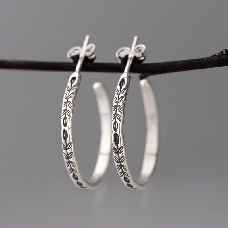 Handmade sterling silver hoop earrings with a hand stamped vine design. The earrings are hanging from a branch to show off the nature inspired motif which is oxidized to add contrast and make the handmade details pop.  These are small everyday silver hoop earrings, a great gift for her!
