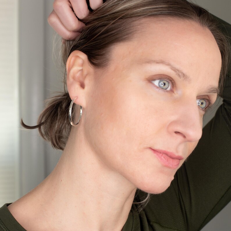 K&ouml;nnte beinhalten: Eine Frau tr&auml;gt silberne Creolen. Die Ohrringe sind schlicht und elegant und verleihen ihrem Look einen Hauch von Eleganz.