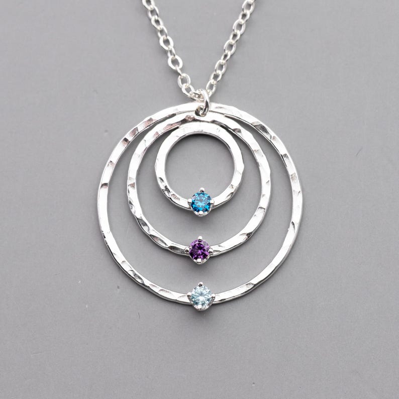 Handmade custom sterling silver grandma necklace is shown against a gray background.  The necklace is made with three circles which are hand hammered and polished to a high shine.  There are birthstones set onto the circles, you can choose the stones and arrangement to create your own custom family necklace to represent three generations.