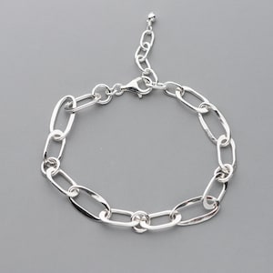 May include: A silver bracelet featuring an oval link chain design. The bracelet has a lobster clasp closure and an adjustable chain. The jewelry is displayed on a gray background.