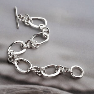May include: A silver bracelet with a hammered finish and a toggle clasp. The bracelet is made of interconnected oval links.