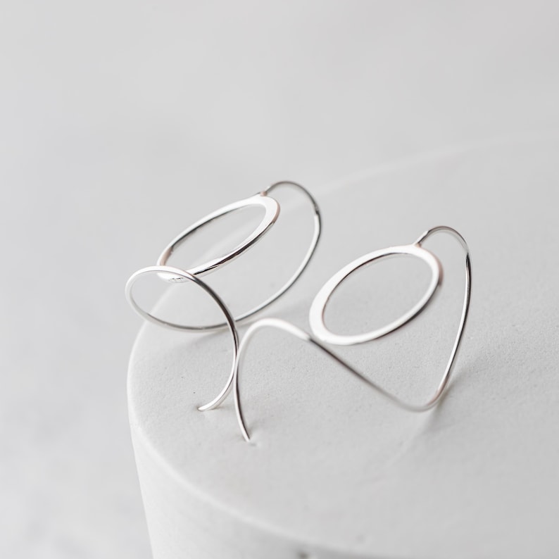 sculptural sterling silver threader earrings are shown from a side angle so you can see the spiral ear wires and how they connect to the hammered sterling silver circles.