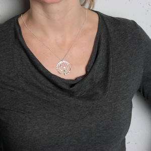 May include: A silver necklace with a pendant featuring three concentric circles, the smallest of which has a green gemstone in the center.