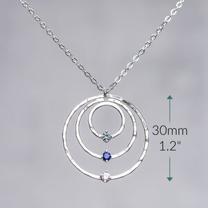 May include: Silver necklace with three hammered circles and three gemstones. The necklace is 1.2 inches long.