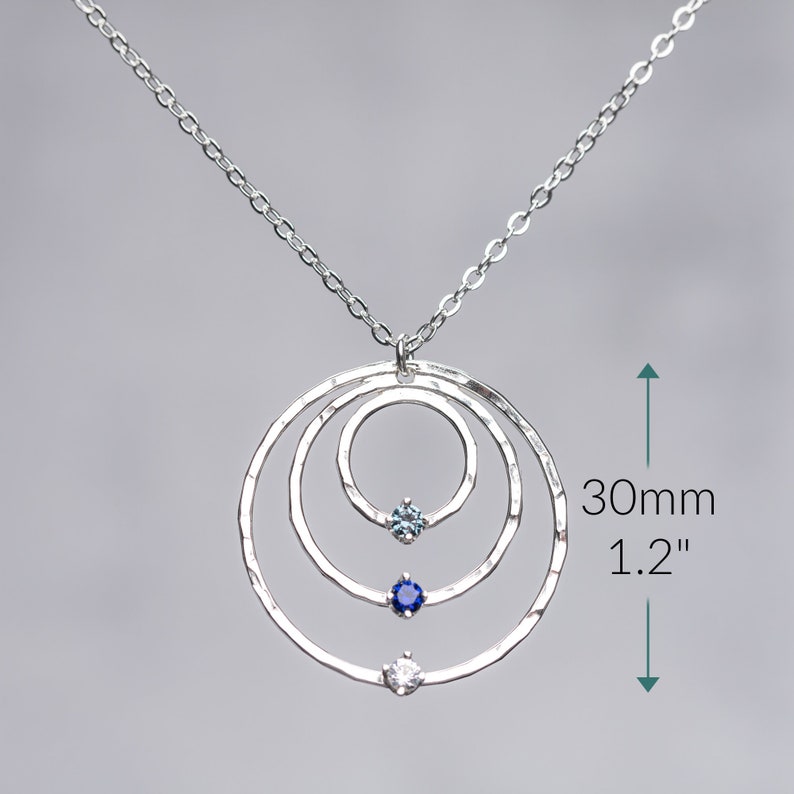 May include: Silver necklace with three hammered circles and three gemstones. The necklace is 1.2 inches long.