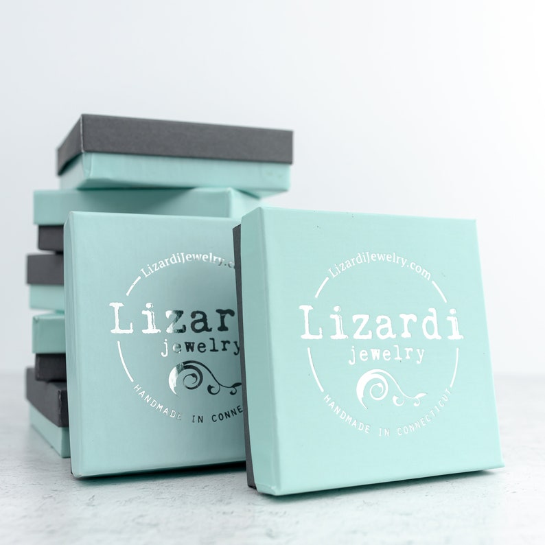 Pode incluir: Pilha de caixas de presente azul claro com um logotipo prateado que diz "Lizardi jewelry" e "feito &agrave; m&atilde;o em Connecticut".