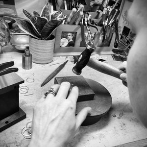 The view from over the shoulder as the earrings are being made.  A woman is pounding on a piece of sterling silver wire with a steel hammer to form and texture the earring.  This gives them their rustic hammered texture, each one a bit different!