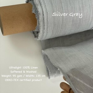 May include: A roll of silver-gray ultralight 100% linen fabric. The fabric is softened and washed, with a weight of 95 gsm and a width of 135 cm. The text "Silver Gray" is written on the fabric. The fabric is an OEKO-TEX certified product.
