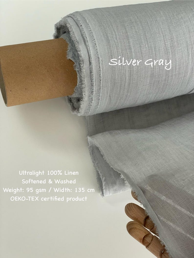 May include: A roll of silver-gray ultralight 100% linen fabric. The fabric is softened and washed, with a weight of 95 gsm and a width of 135 cm. The text "Silver Gray" is written on the fabric. The fabric is an OEKO-TEX certified product.