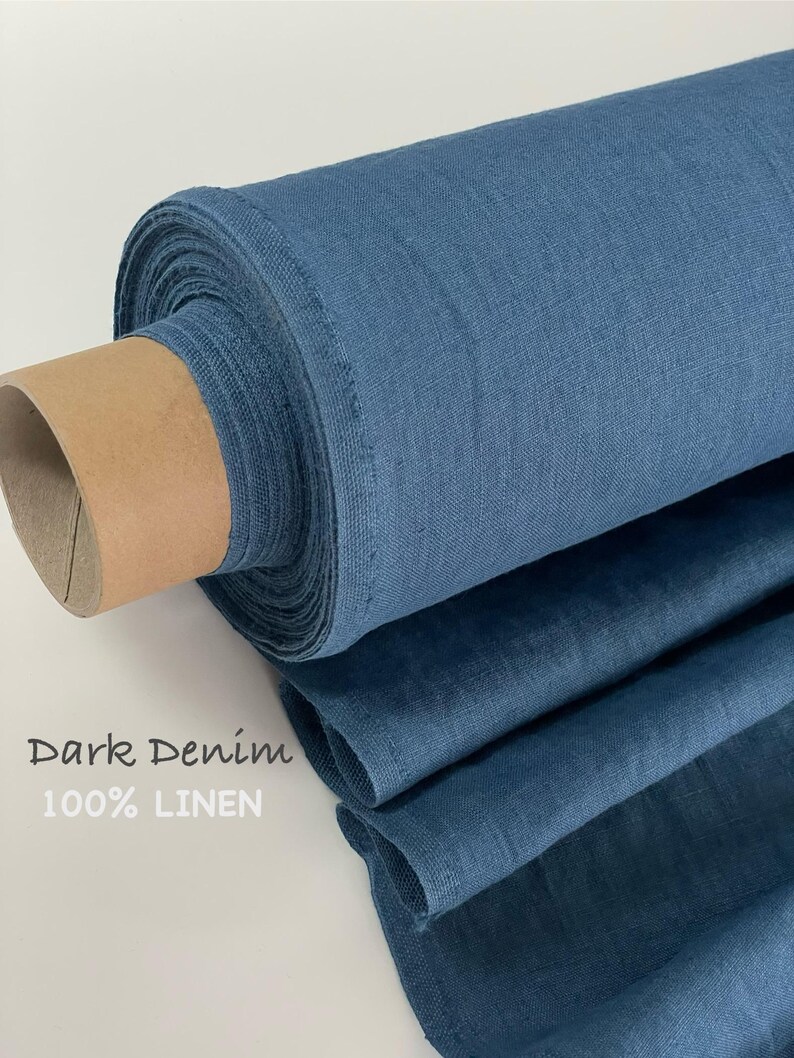 May include: A roll of dark denim blue 100% linen fabric. The textile features a visible woven texture and is wrapped around a cylindrical cardboard core. The text "Dark Denim 100% LINEN" is printed on the left side of the image.