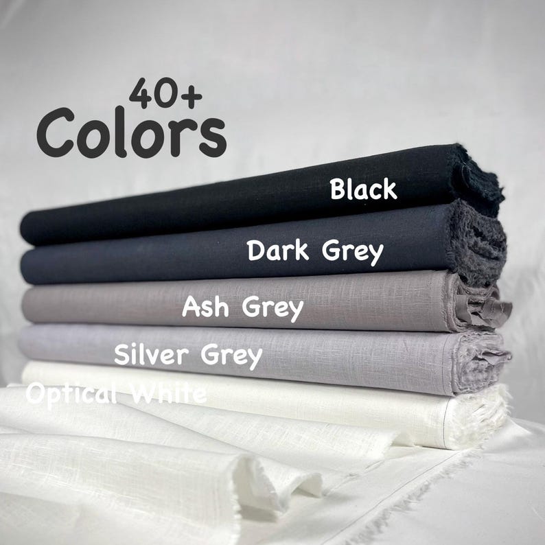 May include: A stack of five fabric bolts in varying shades of neutral tones, labeled with text including 40+ Colors, Black, Dark Grey, Ash Grey, Silver Grey, and Optical White. The fabric has a visible woven texture and frayed edges on the sides.