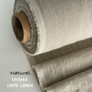 Könnte beinhalten: Eine Rolle aus natürlichem, ungefärbtem 100% Leinenstoff mit sichtbarer Webstruktur und ausgefransten Kanten. Der Stoff ist um eine braune Papprolle gewickelt. Der Text Natural Undyed 100% LINEN ist links in Schwarz aufgedruckt.