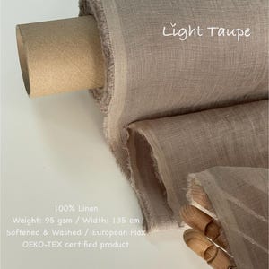 May include: A roll of light taupe 100% linen fabric. The fabric is 135 cm wide and weighs 95 gsm. The text "Light Taupe" is written on the fabric. The fabric is softened, washed, and made from European flax.