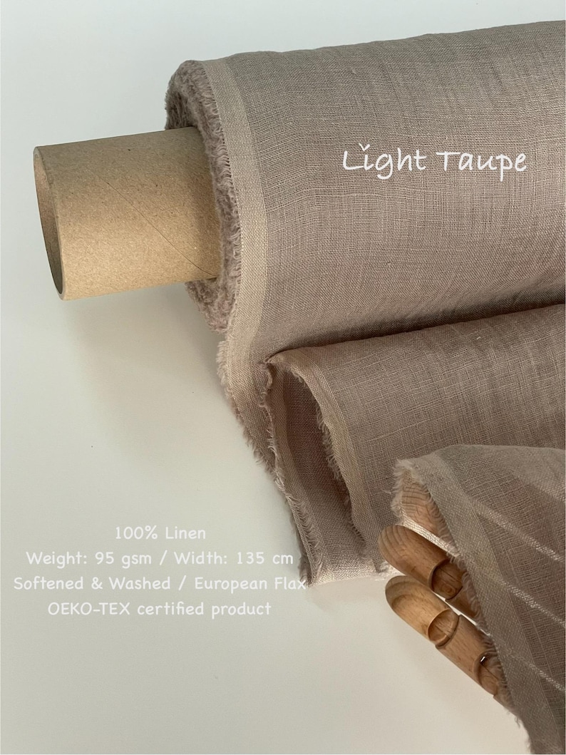 May include: A roll of light taupe 100% linen fabric. The fabric is 135 cm wide and weighs 95 gsm. The text "Light Taupe" is written on the fabric. The fabric is softened, washed, and made from European flax.