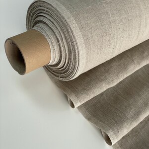 May include: A roll of natural linen fabric in a beige color. The fabric is rolled up and tied with a brown paper band.