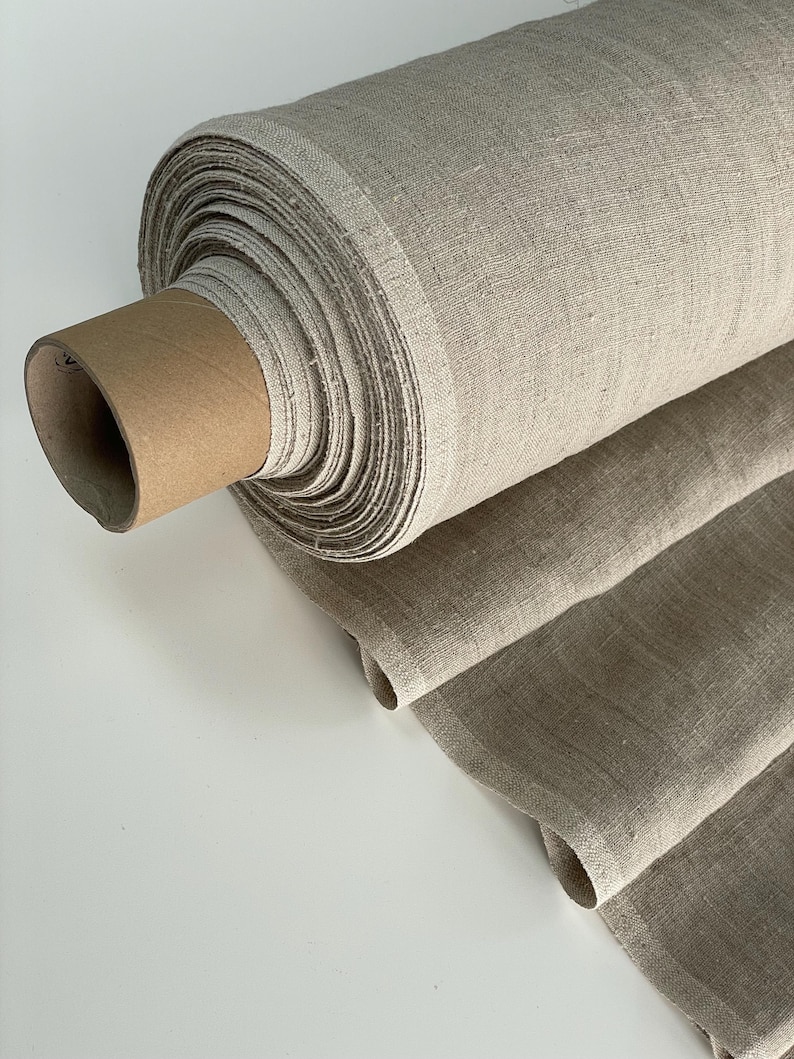 May include: A roll of natural linen fabric in a beige color. The fabric is rolled up and tied with a brown paper band.