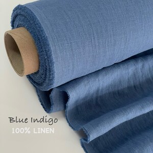 May include: A roll of blue indigo 100% linen fabric with a visible woven texture and frayed edges. The fabric is wrapped around a cylindrical cardboard core, with a portion of the material unrolled to display its drape and consistent blue color.