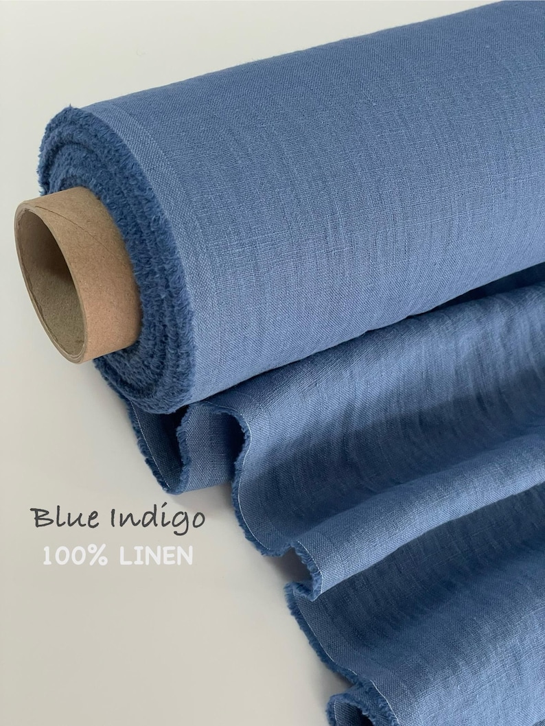 May include: A roll of blue indigo 100% linen fabric with a visible woven texture and frayed edges. The fabric is wrapped around a cylindrical cardboard core, with a portion of the material unrolled to display its drape and consistent blue color.