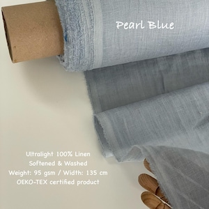 May include: A roll of pearl blue ultralight 100% linen fabric. The fabric is softened and washed, with a weight of 95 gsm and a width of 135 cm. The text "Pearl Blue" is visible on the fabric. The fabric is an OEKO-TEX certified product.