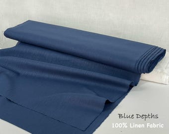May include: A bolt of solid dark blue linen fabric with a visible woven texture. The fabric is folded over itself, creating soft drapes. Text printed on the lower right corner reads: Blue Depths 100% Linen Fabric.