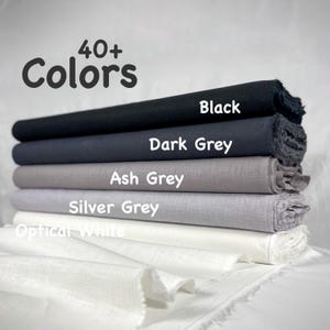 May include: A stack of five fabric bolts in a gradient of shades including black, dark grey, ash grey, silver grey, and optical white. The text 40+ Colors is displayed at the top, with individual labels identifying each fabric color layer.