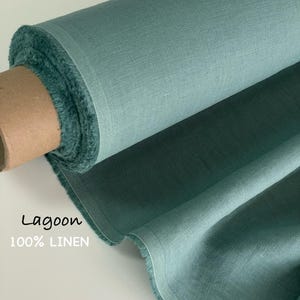 Puede incluir: Un rollo de tela 100% lino en color laguna. El tejido presenta una textura tejida visible y un acabado mate suave. La tela está enrollada alrededor de un núcleo de cartón, mostrando un tono verde azulado constante en todo el material.